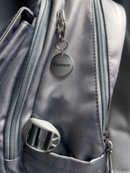 Personalised metal keychain with name Eleanor attached to grey backpack zip, custom engraved bag tag
