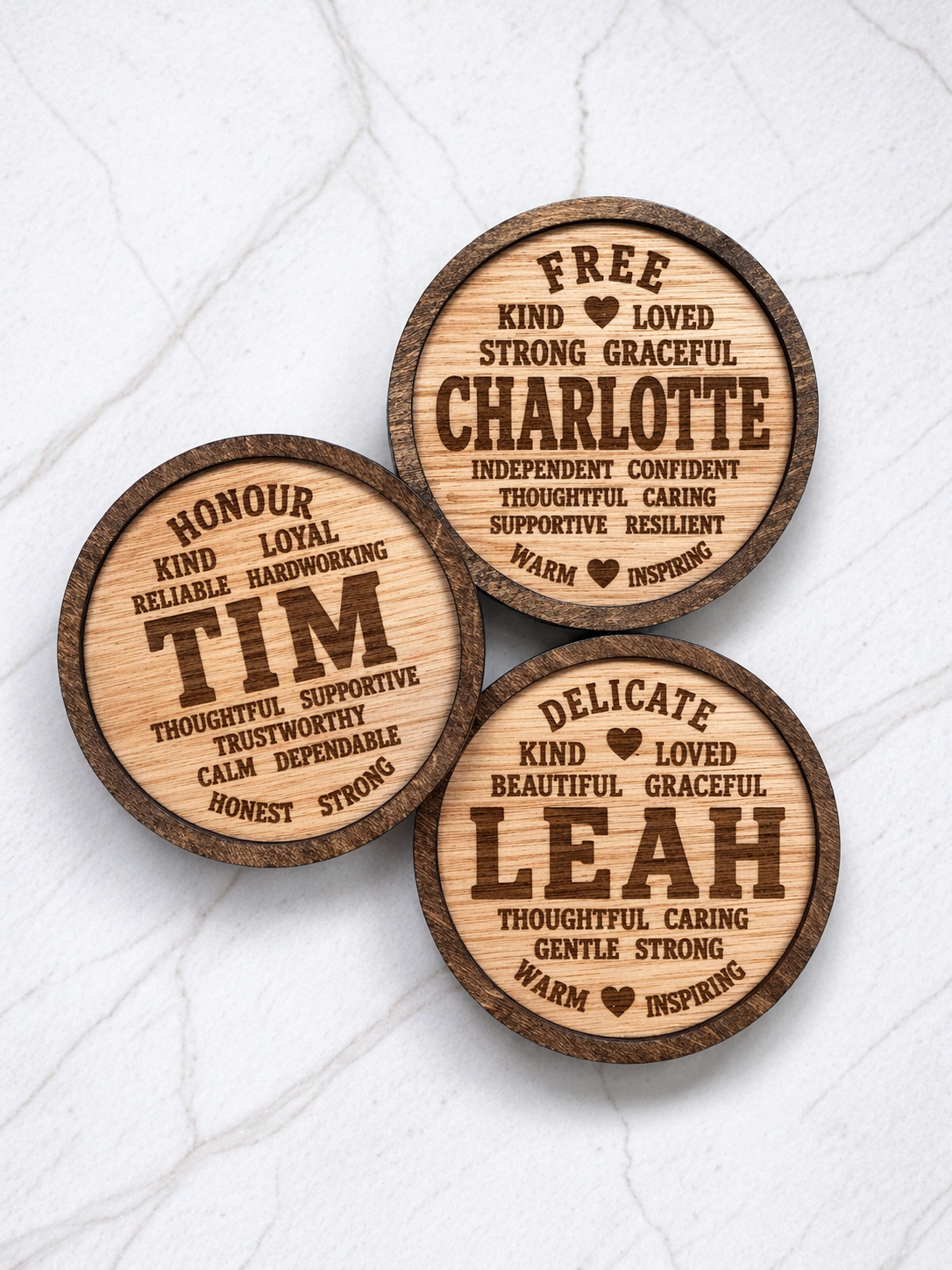 Set of personalised engraved wooden coasters featuring name meanings and positive words, displayed stacked on a marble background