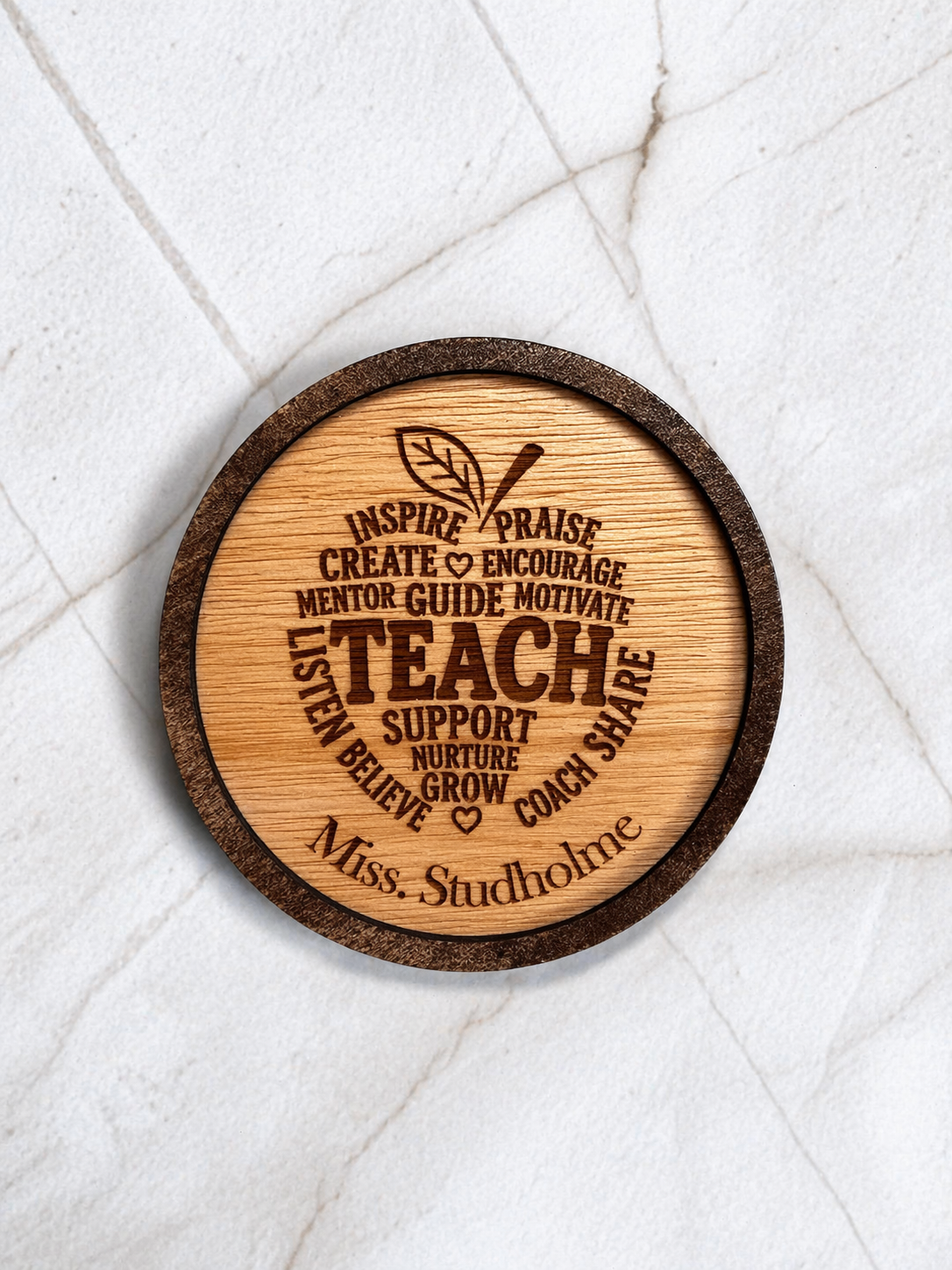Close up of personalised engraved wooden teacher coaster with inspirational wording and custom name on marble background