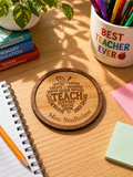 Engraved wooden teacher coaster personalised with name displayed on a classroom desk with pens, books and plant in warm natural light