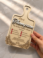 Hand holding personalised wooden teacher recipe plaque engraved with name and floral design on marble background