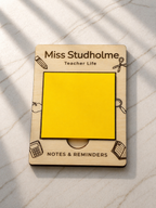 Close-up of engraved wooden sticky note holder personalised with teacher name, different engraved designs such as a book, calculator, pencil and more. Sticky notes on marble surface