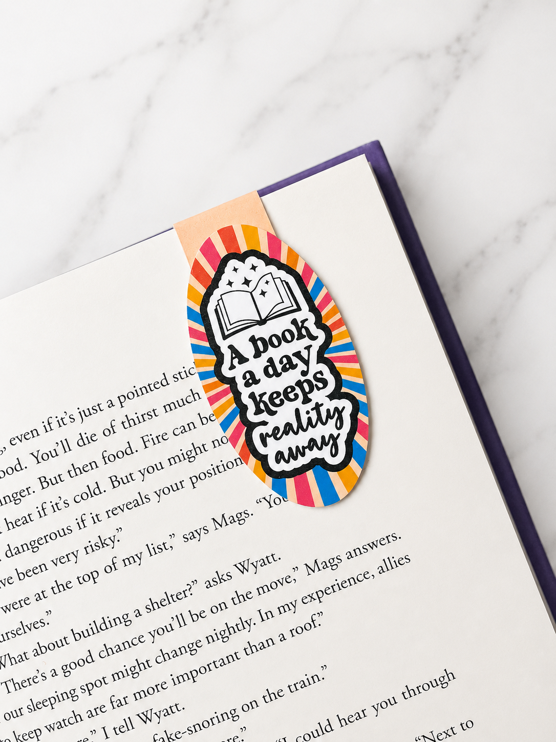 Colourful magnetic bookmark with reading quote clipped onto a book page