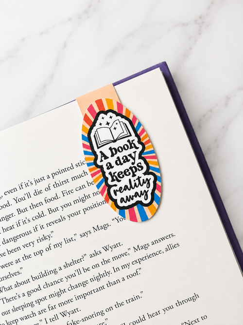 Colourful magnetic bookmark with reading quote clipped onto a book page