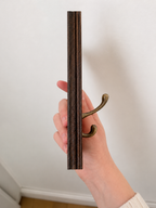 Hand holding a decorative dog lead holder on the side with one hook against a plain wall.