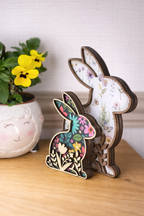 Side view of decorative wooden bunny figures with floral patterns on the inside with wooden flower cutouts layered on top. There are 2 sizes and designs of pattern in the photo.