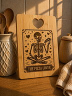 Bamboo chopping board with skeleton holding pizza engraving styled in warm kitchen setting with utensils and soft lighting