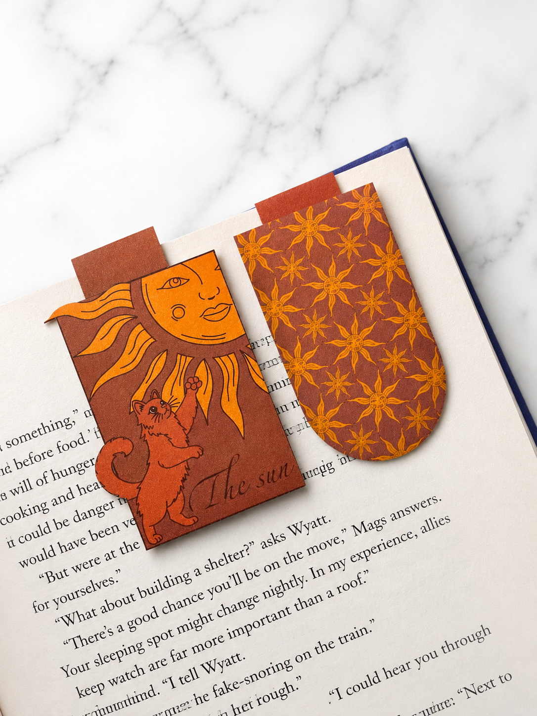 Two magnetic bookmarks with sun designs placed on open book pages