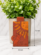 Magnetic bookmark featuring a cat reaching toward a stylised sun illustration in warm orange tones