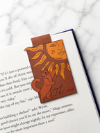 Magnetic bookmark with sun and cat illustration holding pages in an open book