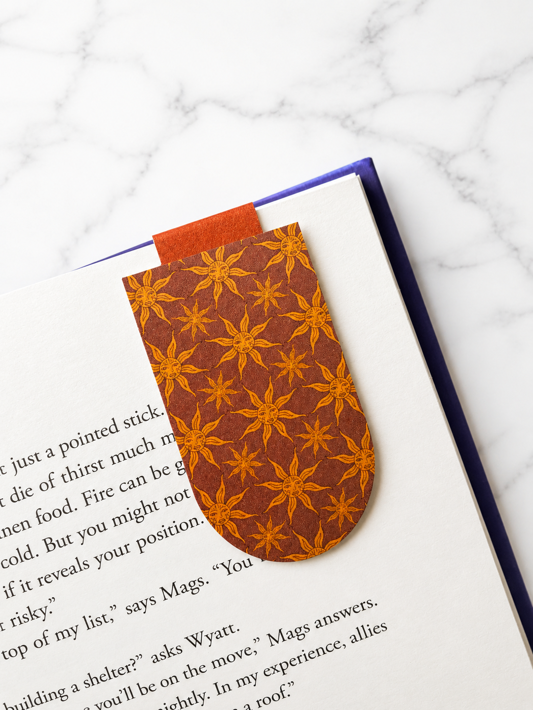 Magnetic bookmark with repeating sun pattern clipped onto a book page
