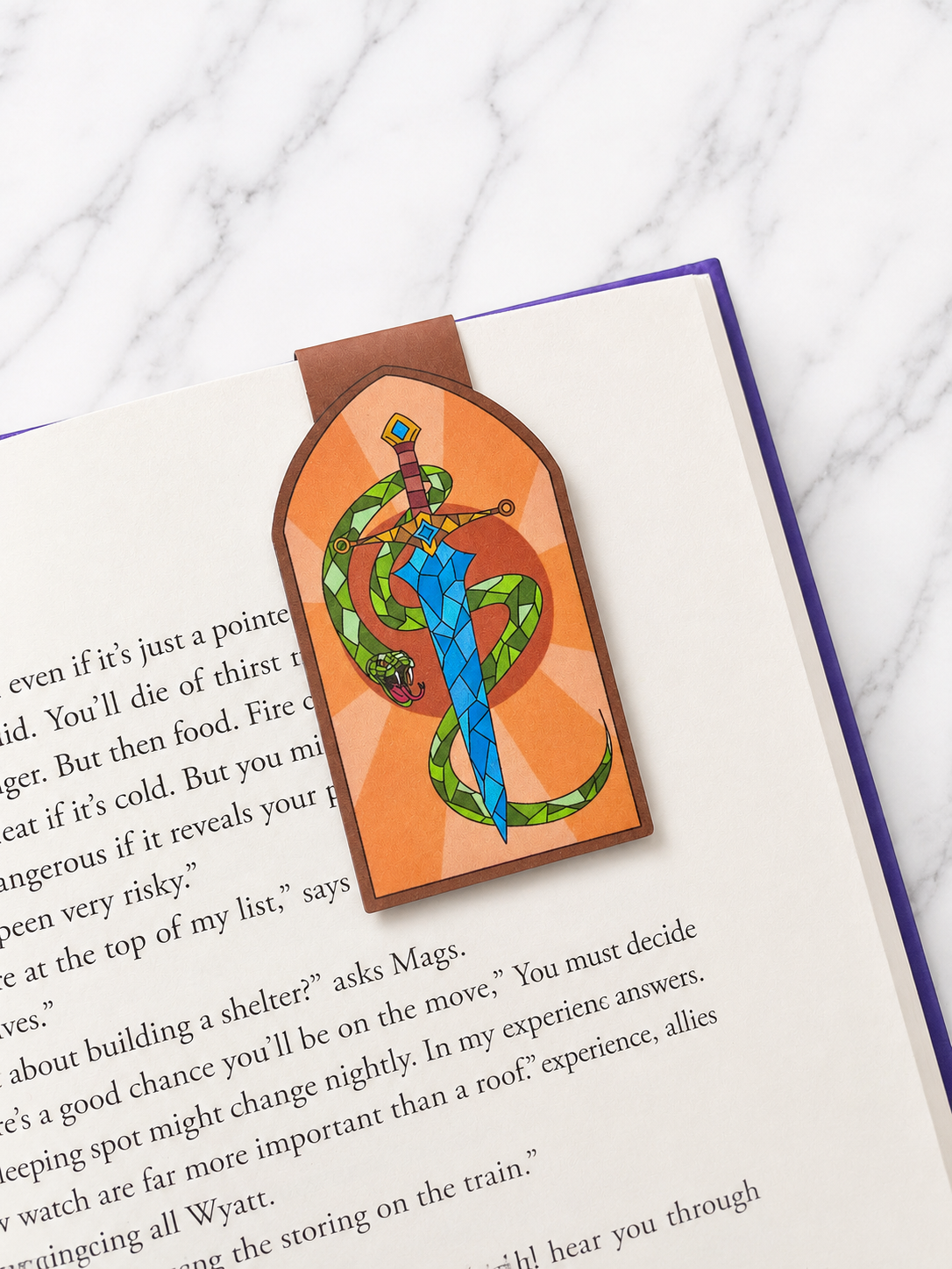 Magnetic bookmark with sword and snake design clipped onto an open book showing how it marks pages