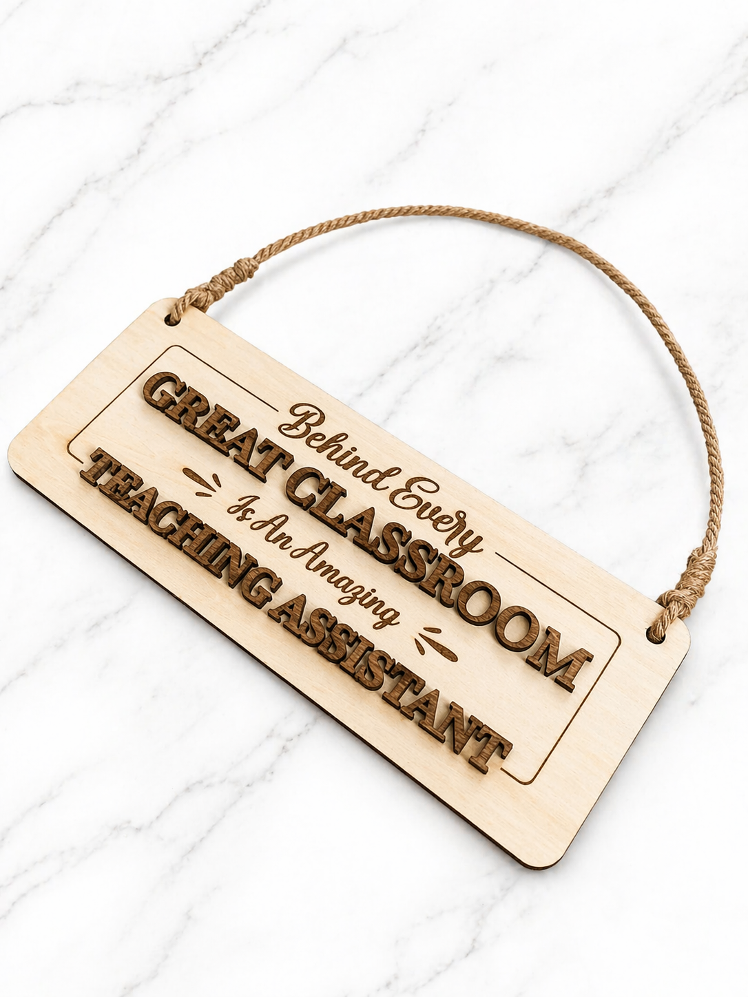 Wooden hanging sign engraved with “Behind Every Great Classroom Is An Amazing Teaching Assistant” on marble background