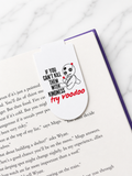 Magnetic bookmark clipped onto the top of an open book page featuring a voodoo doll design and humorous text, demonstrating how it securely marks pages