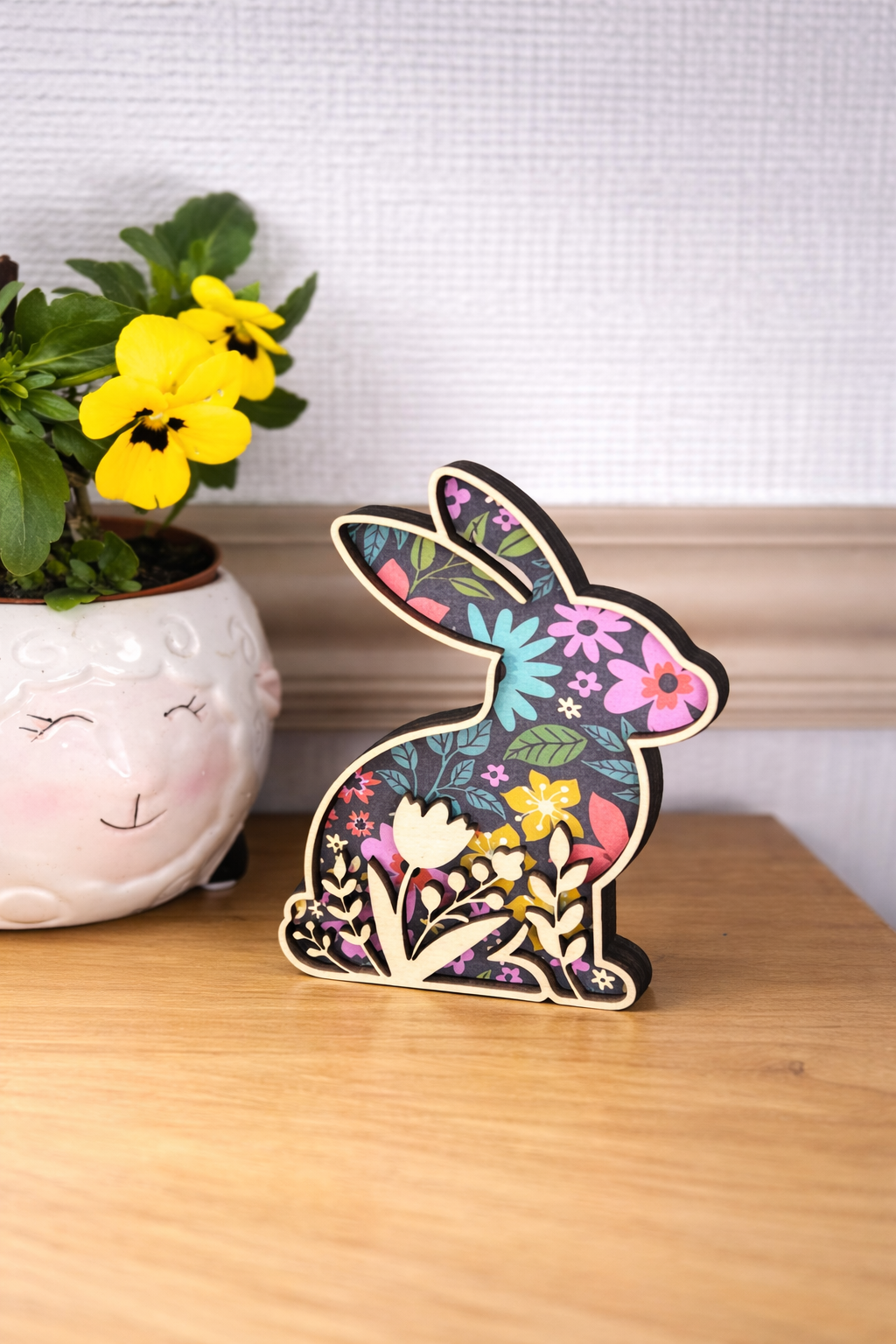 Decorative rabbit figurine with floral patterns on a dark background and a cut out of flowers following the bottom silhouette of the rabbit.