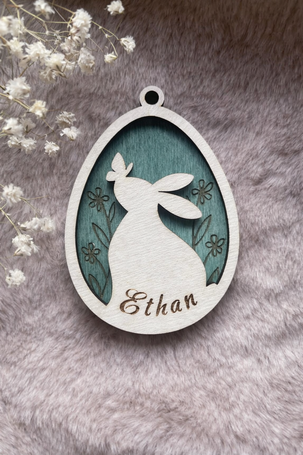 Wooden tag with a bunny and butterfly inside an egg with floral background stained forest green. On the bottom is space for a personalised name.