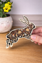 Wooden rabbit ornament with floral patterns held by a hand on a wooden surface.