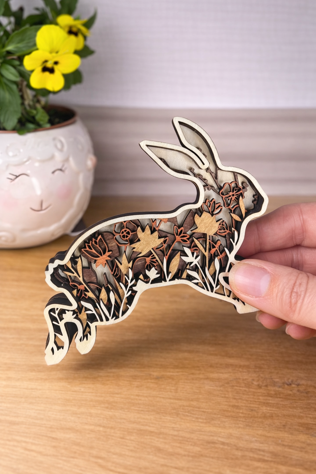 Wooden rabbit ornament with floral patterns held by a hand on a wooden surface.