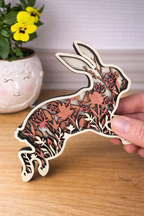 Wooden rabbit ornament with floral patterns held by a hand on a wooden surface.