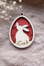 Wooden tag with a bunny and butterfly inside an egg with floral background stained red. On the bottom is space for a personalised name.