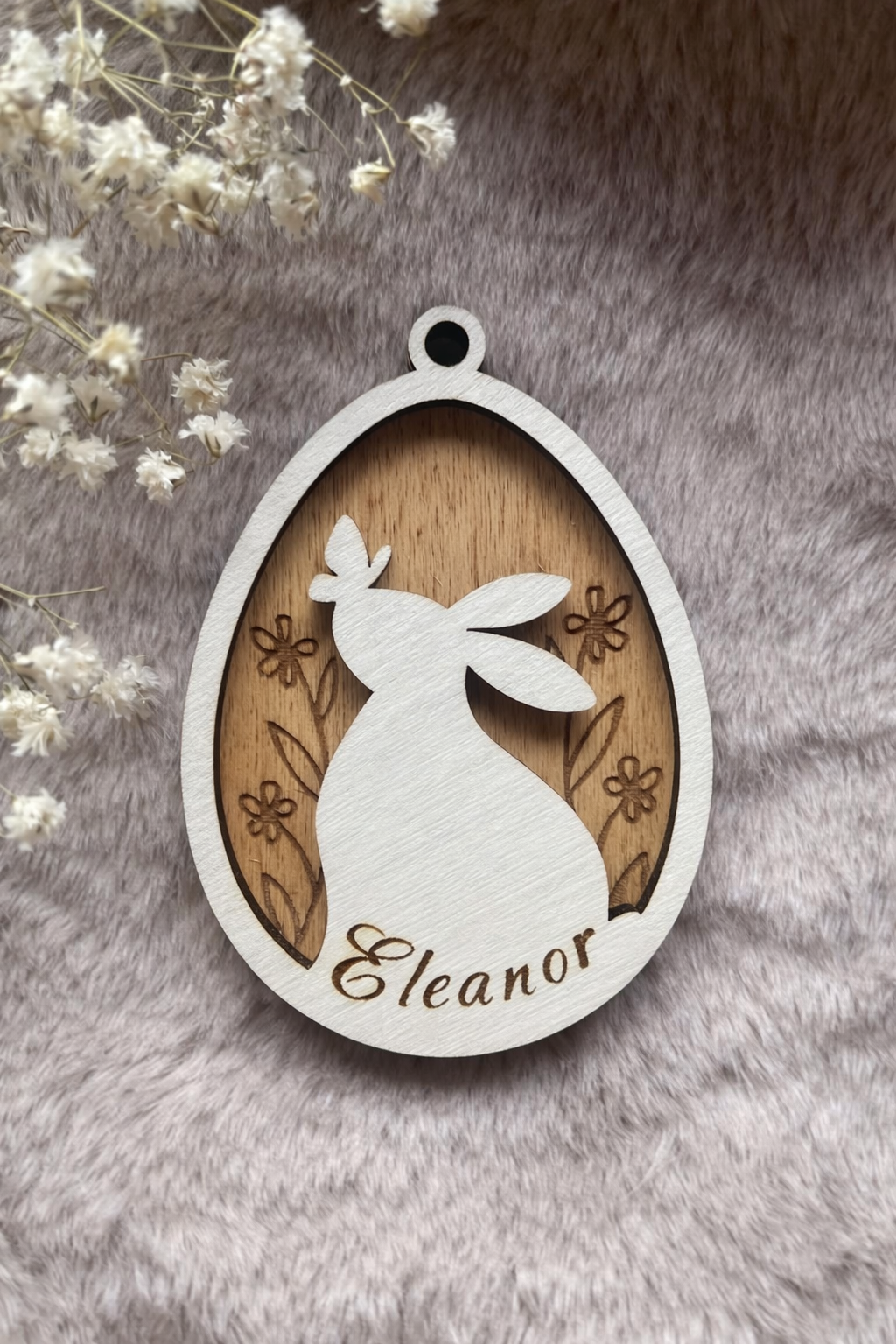 Wooden tag with a bunny and butterfly inside an egg with floral background stained teak/ light brown. On the bottom is space for a personalised name.